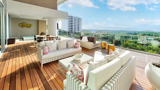A modern outdoor living area with a wooden deck, white sofas, and a dining table.