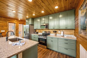 A kitchen with wooden cabinets, granite countertops, stainless steel appliances, and a window with blinds. - Mountain Views+Hot Tub+Fire Pit+4 Mi to Pigeon Forge (Sevierville)
