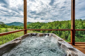 Ein Whirlpool mit Holzterrasse und Metallgeländer, umgeben von üppiger Vegetation und einer Bergkulisse.