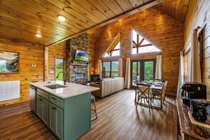 Geräumiges Blockhaushaus-Interieur mit Küche, Essbereich und Kamin aus Stein.