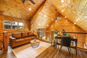 L’intérieur chaleureux d’un chalet avec un plafond en bois, un canapé en cuir, une table basse ronde et un bureau avec une chaise.