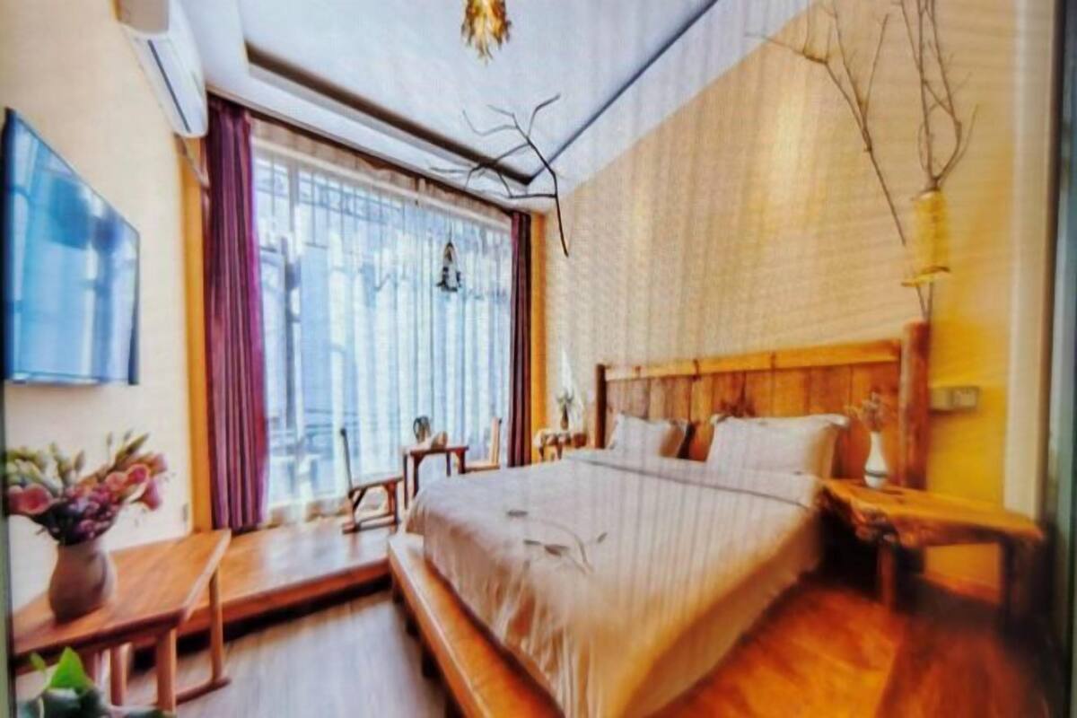 A bedroom with a large bed, a wooden bench, a desk, and a window with curtains.
