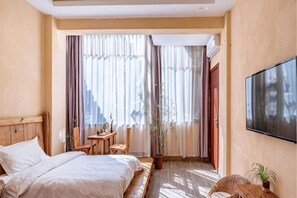 A hotel room with a bed, a TV, a desk, and a window with curtains. - Beginner's Mind in Dali Art Theme Hotel (Dali City)