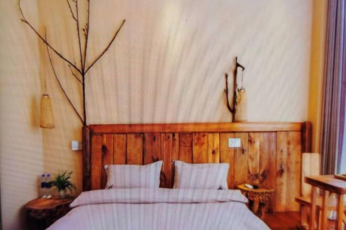 A bedroom with a wooden headboard, a bed with a striped bedspread, a nightstand with a lamp, and a small table with a chair.