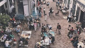 An outdoor public space with tables and chairs, people sitting and walking, and a staircase leading to an upper level.