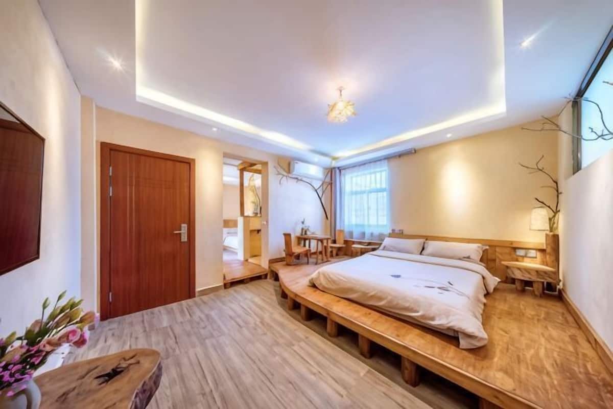 A modern bedroom with a wooden bed, bedside tables, a desk, and a large window.