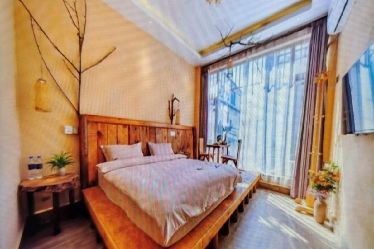 A bedroom with a wooden bed, a bench, a bedside table, a potted plant, and a window with curtains.