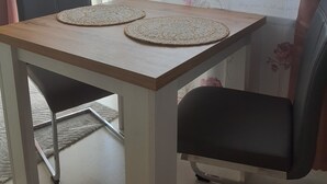 Ein Esstisch mit zwei Platzsets, einem Stuhl und einem Fenster mit floralem Vorhang.