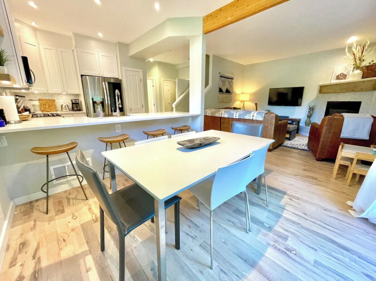 A modern kitchen with white cabinets, a stainless steel refrigerator, and a dining area with a white table and chairs.