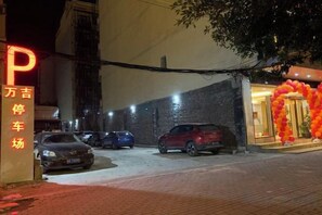 A parking lot with several cars parked, a building entrance with a red arch, and a sign with illuminated letters. - Jingxi Wanji Hotel (Jingxi)