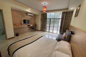 A hotel room with a large bed, a desk with a chair, a television, and a view of the outdoors. - Jingxi Wanji Hotel (Jingxi)