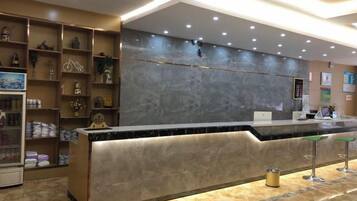 Zona de recepción de un hotel con mostrador de mármol, estanterías con artículos de cortesía y un diseño moderno.