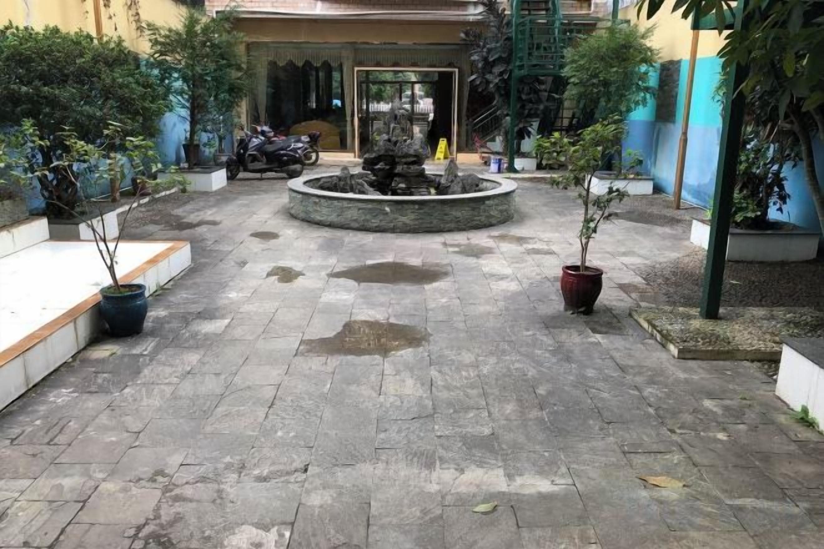 Une cour avec une fontaine, des plantes en pot et une moto garée au fond.