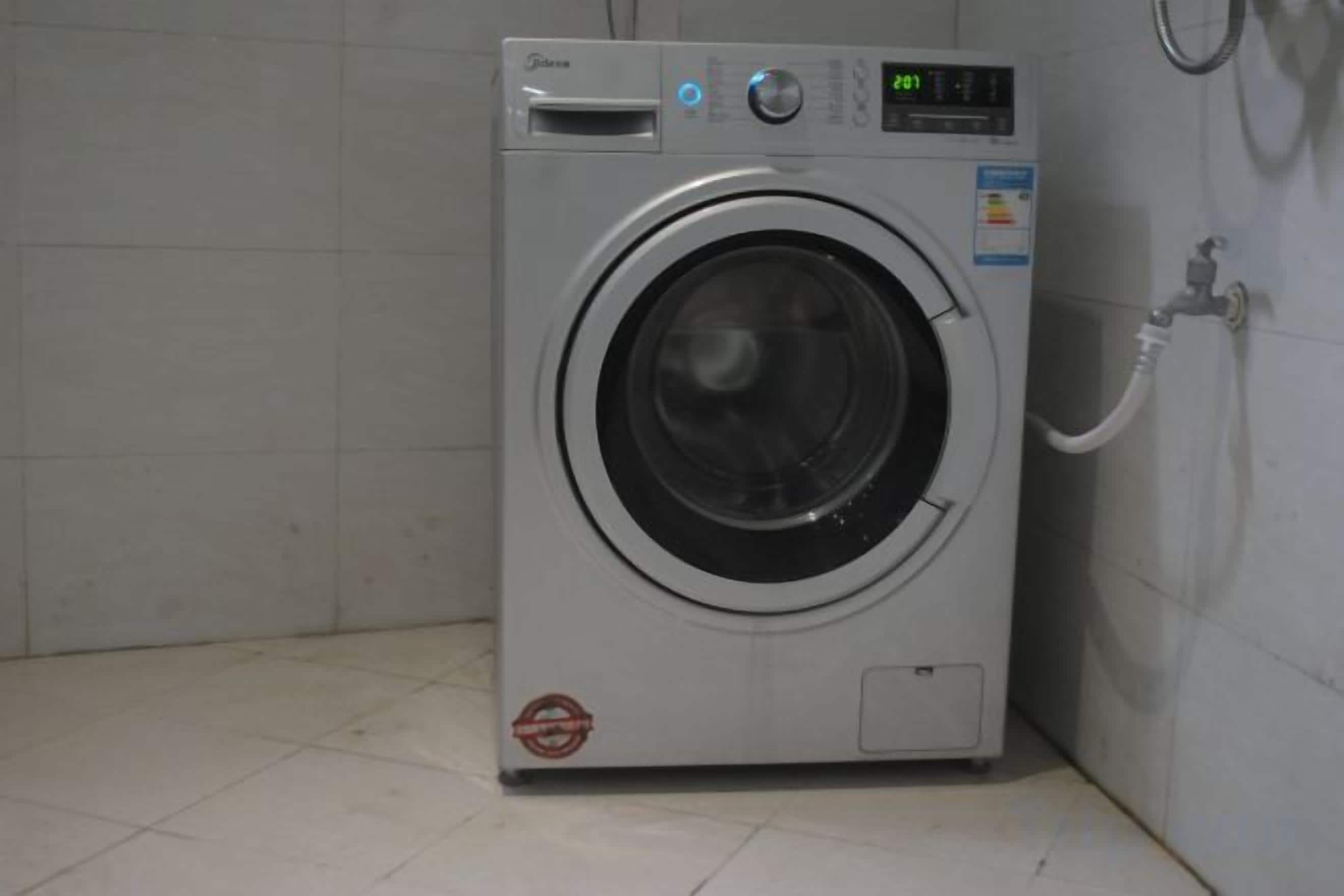 Una lavadora de carga frontal con pantalla digital, panel de control y manguera de entrada de agua.