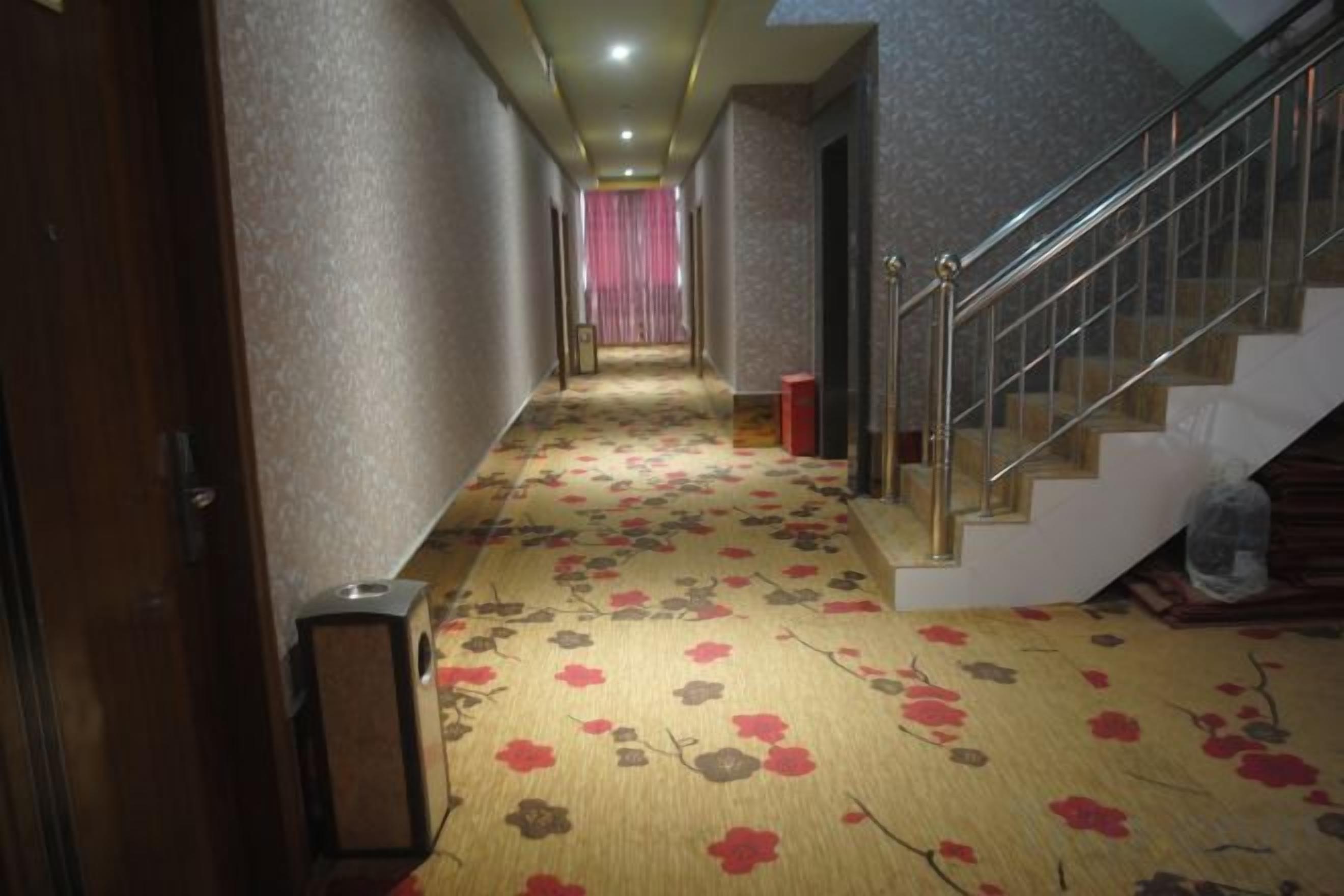 Un couloir d'hôtel avec un revêtement de sol en moquette, un escalier et une porte sur la gauche.