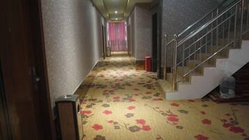 Un couloir d'hôtel avec un revêtement de sol en moquette, un escalier et une porte sur la gauche.