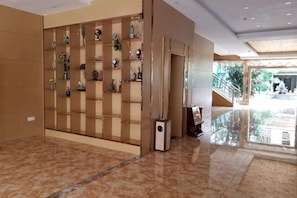 A hotel lobby with a tiled floor, a wall of decorative items, and a staircase leading to an outdoor area.