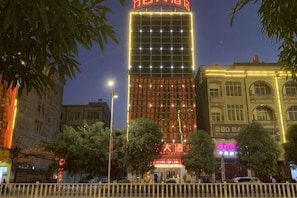 A tall building with illuminated signage, a gated entrance, and surrounding trees.