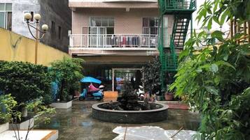 A courtyard with a fountain, potted plants, and a multi-story building with balconies.