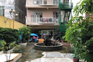 Un patio con una fuente, plantas en macetas y un edificio de varios pisos con balcones.