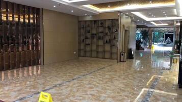 Un vestíbulo de hotel con piso de mármol pulido, una mesa de recepción y una pared con cuadros enmarcados.
