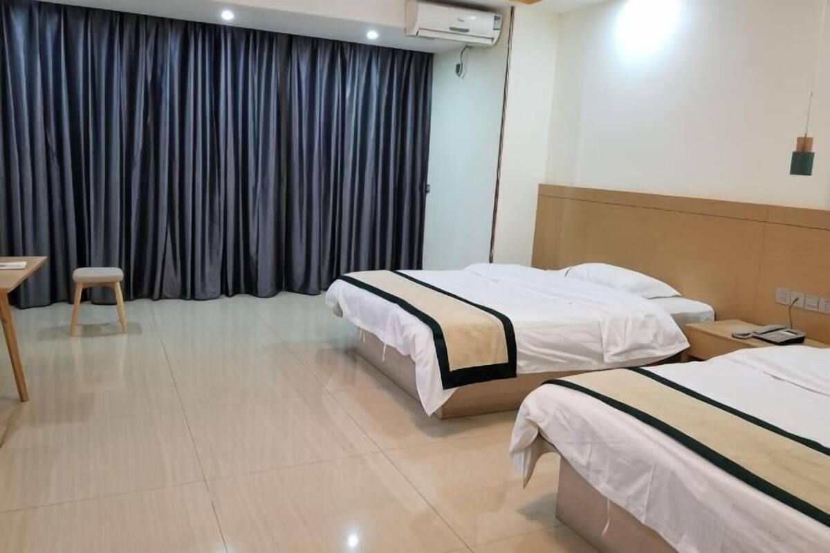 Hotellihuone, jossa on kaksi sänkyä, työpöytä, tuoli ja suuri ikkuna, jossa on verhot.