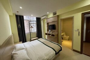 A hotel room with a bed, a TV mounted on the wall, a window with curtains, and a door leading to the bathroom. - Jingxi Wanji Hotel (Jingxi)