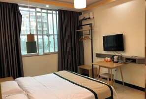 Une chambre d’hôtel comprenant un lit, un bureau avec une chaise, une télévision et une fenêtre avec des rideaux.
