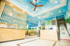 A hotel lobby with a reception desk, a ceiling fan, a staircase, and a mural of palm trees. - Nongzai Guesthouse (Sanya Wuzhizhou Island Houhai) (Sanya)