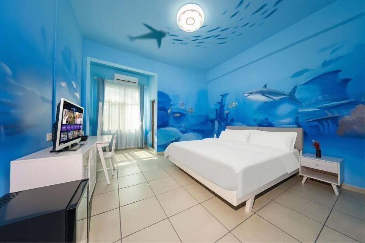 Une chambre avec un grand lit, un téléviseur posé sur un meuble et une fresque murale représentant des poissons et des requins.