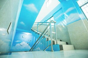 A staircase with metal railings leading to a higher floor, a wall with a mural of clouds and birds, and a window allowing natural light. - Nongzai Guesthouse (Sanya Wuzhizhou Island Houhai) (Sanya)