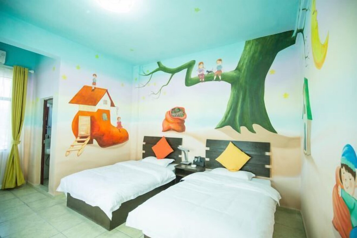 A room with two beds, a mural of a tree with children on it, and a window with curtains.