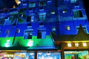 A multi-story building with illuminated windows and a restaurant with a traditional roof. - Nongzai Guesthouse (Sanya Wuzhizhou Island Houhai) (Sanya)