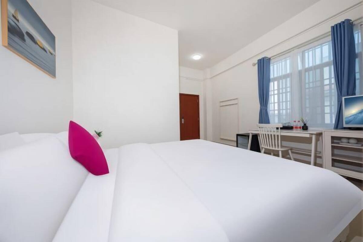Une chambre d’hôtel avec un grand lit, un bureau avec une chaise, une télévision et une fenêtre avec des rideaux.