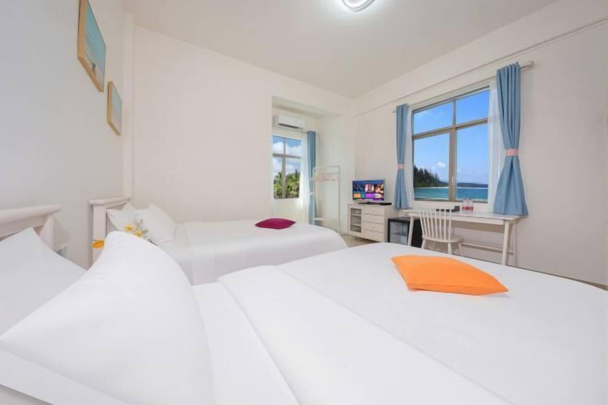 Une chambre d’hôtel avec deux lits, un bureau, une télévision et une fenêtre donnant sur la mer.