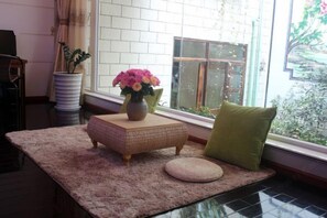 A cozy seating area with a cushioned bench, a small table with a vase of flowers, and a window with a view of greenery. - Dali Ancient City Xiaoqiang Craft Theme Homestay (Dali City)
