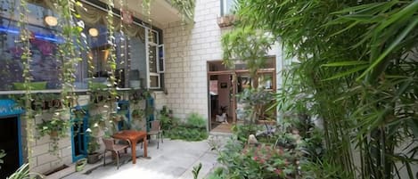 Un jardín interior con plantas colgantes, una mesa de madera y sillas.