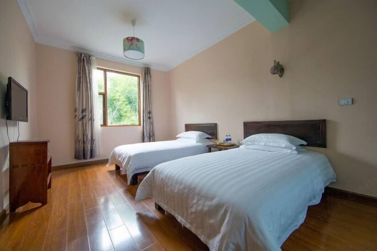 A hotel room with two beds, a wooden floor, a television, and a window with curtains.