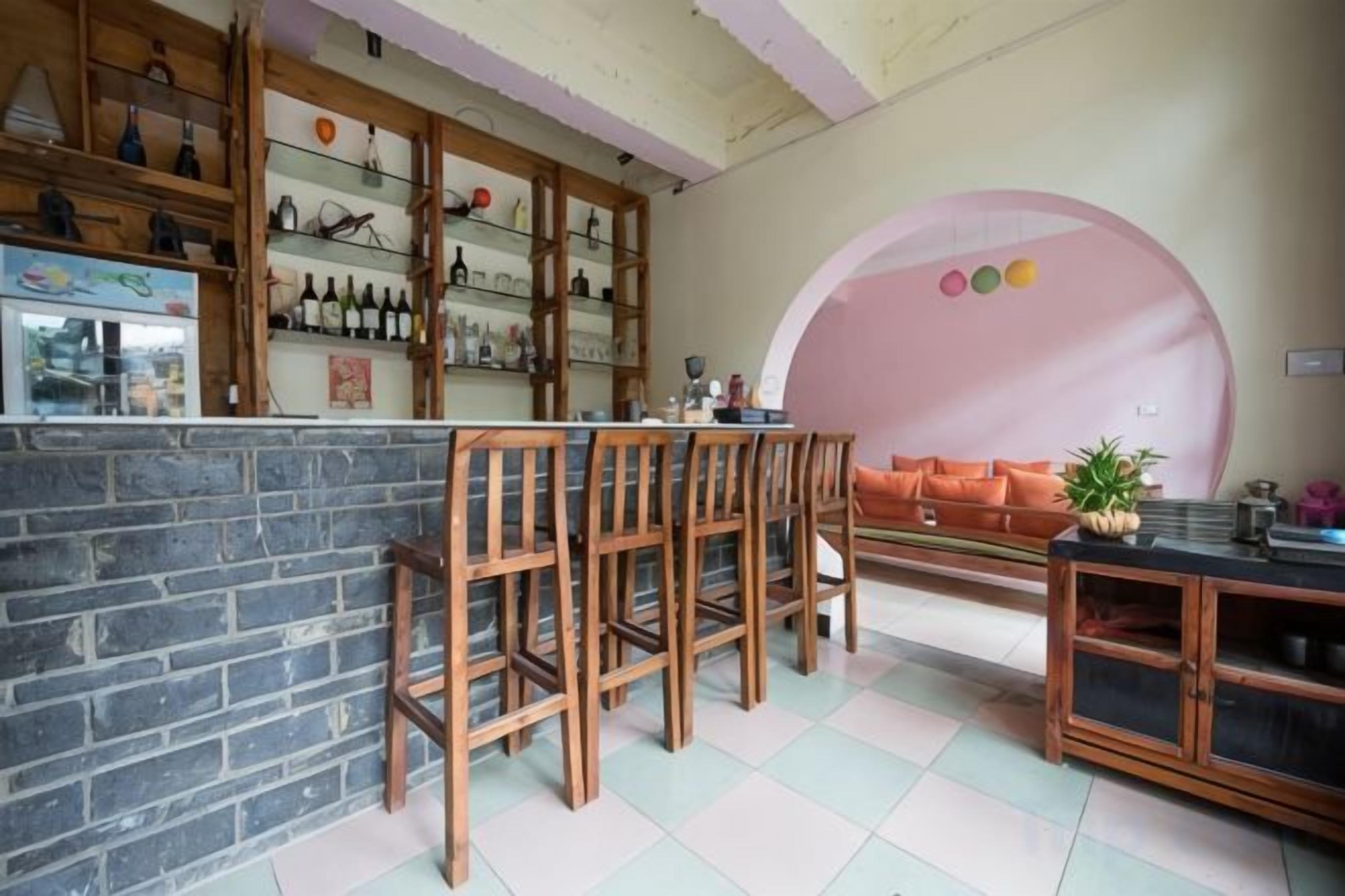 Een bar met een bakstenen toonbank, houten krukken en een zithoek met een bank en een tafel.