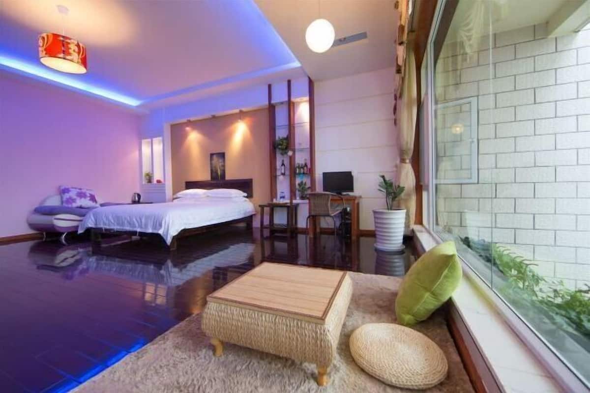 A modern hotel room with a bed, a desk, a chair, a small table, and a window with a view.