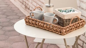 A white table with a woven tray holding mugs and a basket of cards, set against a brick wall. - Exclusiva Casa en una de las Mejores Zonas de Mendoza (Buenos Aires)