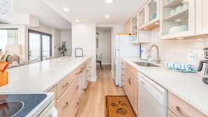A modern kitchen with white cabinetry, a central island, and a view into the dining area. - Ocean Front Condo with Sunrise Views (Ocean City)