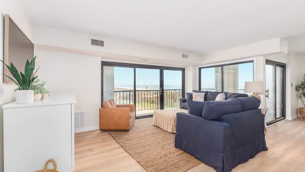 A modern living room with a sofa, a small table, a plant, and a view of the outdoors. - Ocean Front Condo with Sunrise Views (Ocean City)