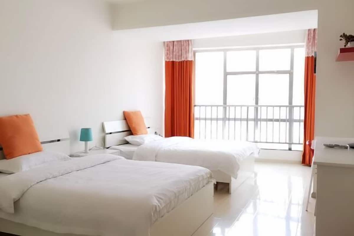 A hotel room with two beds, a nightstand, a lamp, and a window with curtains.