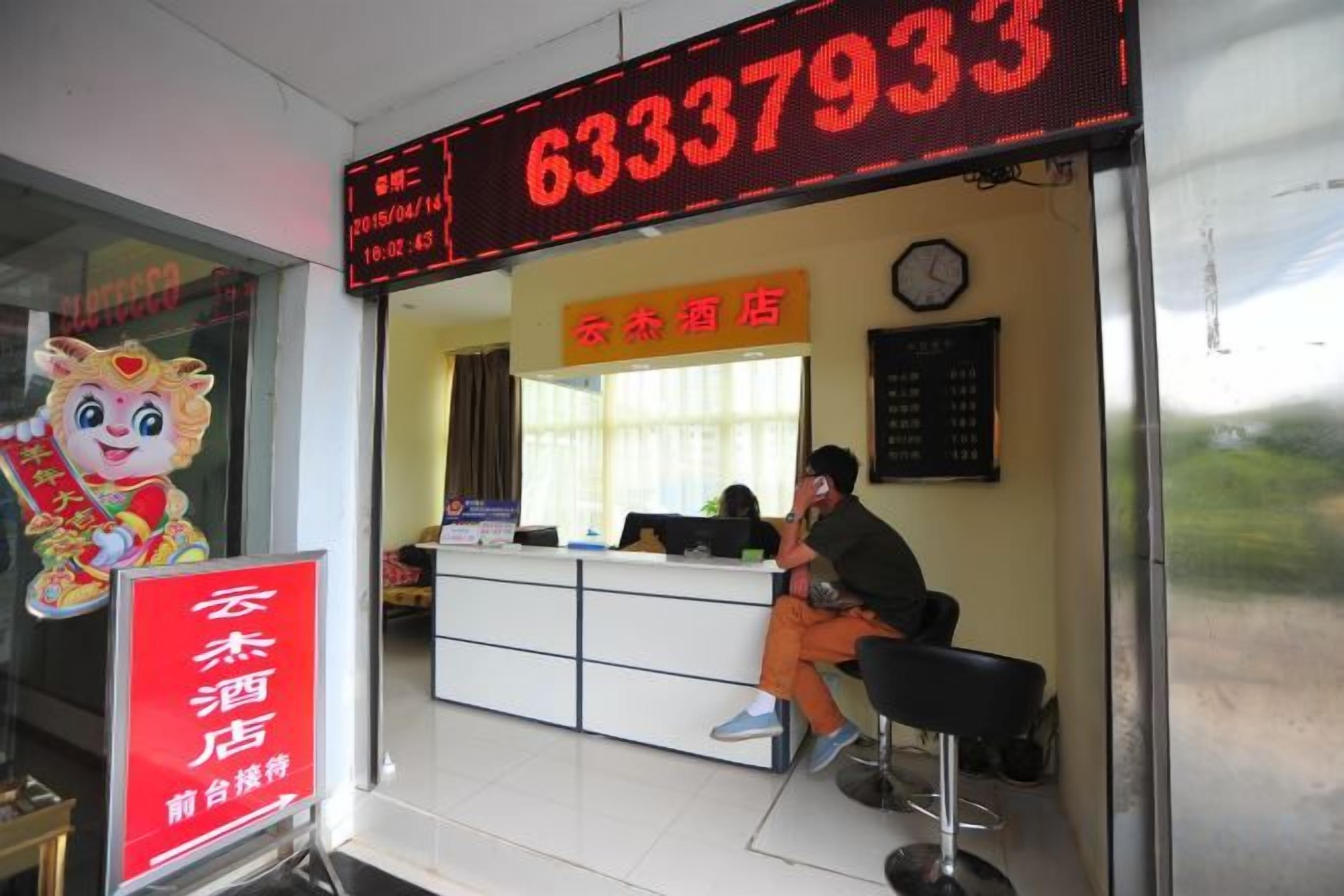 A hotel reception area with a digital display showing the number 63337933. There is a receptionist seated at the desk, and a sign with Chinese characters.