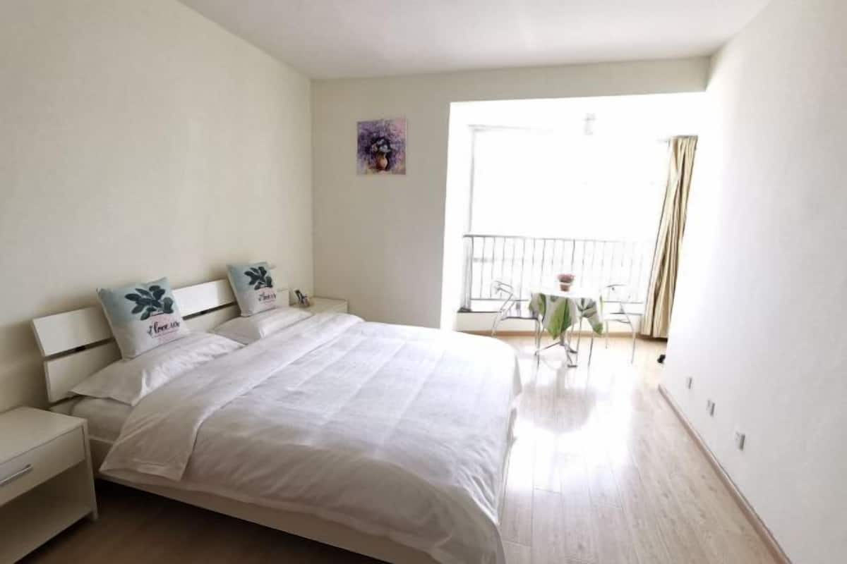 A bedroom with a bed, nightstands, a small table, and a balcony with a railing.