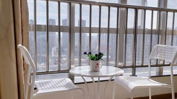 A balcony with a view of a cityscape, two white chairs, a small round table with a potted plant, and a white radiator. - Yunjie Apartment Hotel (Kunming)