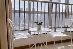 Un balcon donnant sur un paysage urbain, deux chaises blanches, une petite table ronde avec un pot de fleurs et un radiateur blanc.