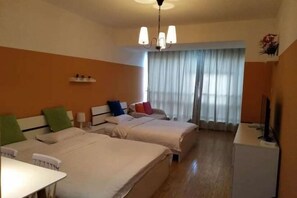 A hotel room with two beds, a desk, a television, and a window with curtains.