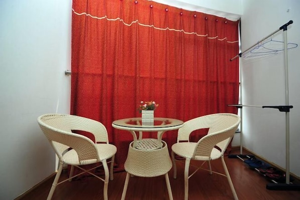 Une petite pièce avec un rideau rouge, une table ronde en verre et deux chaises en osier, ainsi qu’un lampadaire.